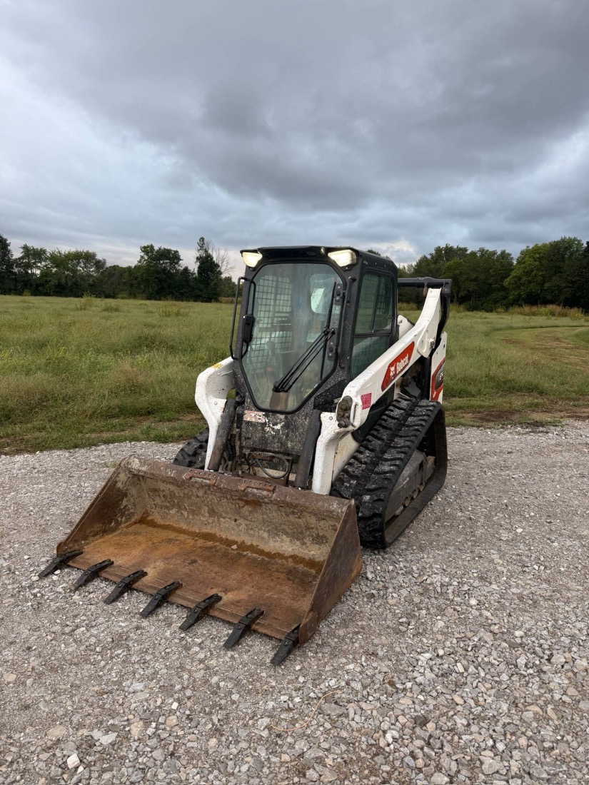 White 2021 Bobcat T64 compact track loader on new tracks with a fresh-toothed bucket, parked on gravel in front of a field