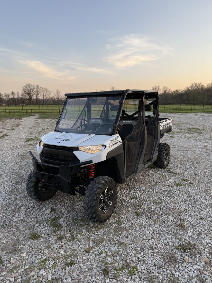 White Polaris Ranger Crew XP 1000 with roof, full windshield and aftermarket wheels on gravel