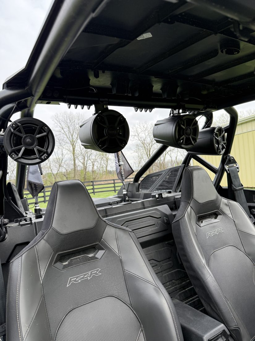 Four aftermarket speaker pods mounted overhead on a Polaris RZR roll cage