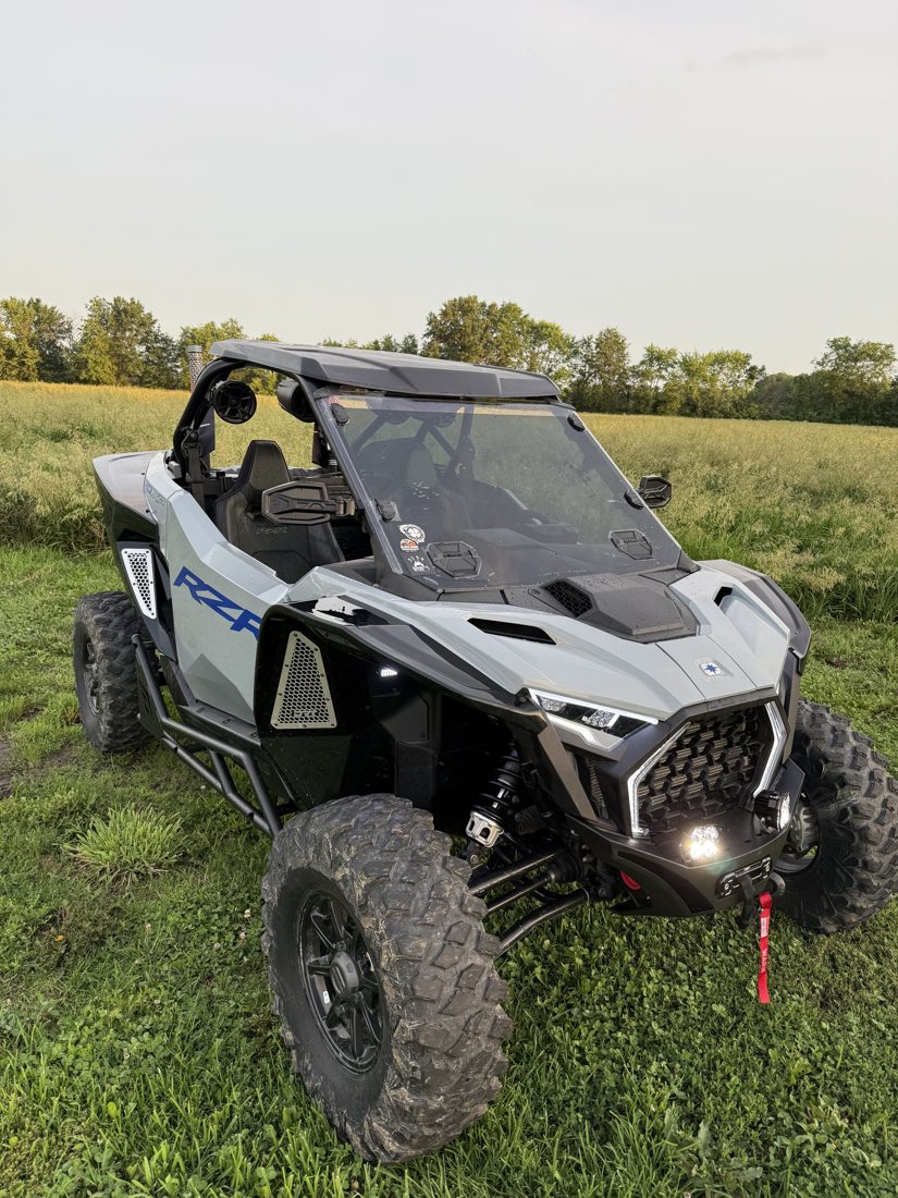 Gray Polaris RZR Pro XP with overhead audio pods, LED lighting and front bumper, parked in a field